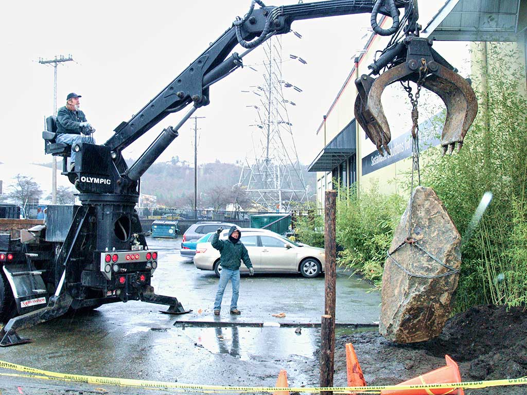 Crane lowering a large rock in front of the new Urbanata retail store.
