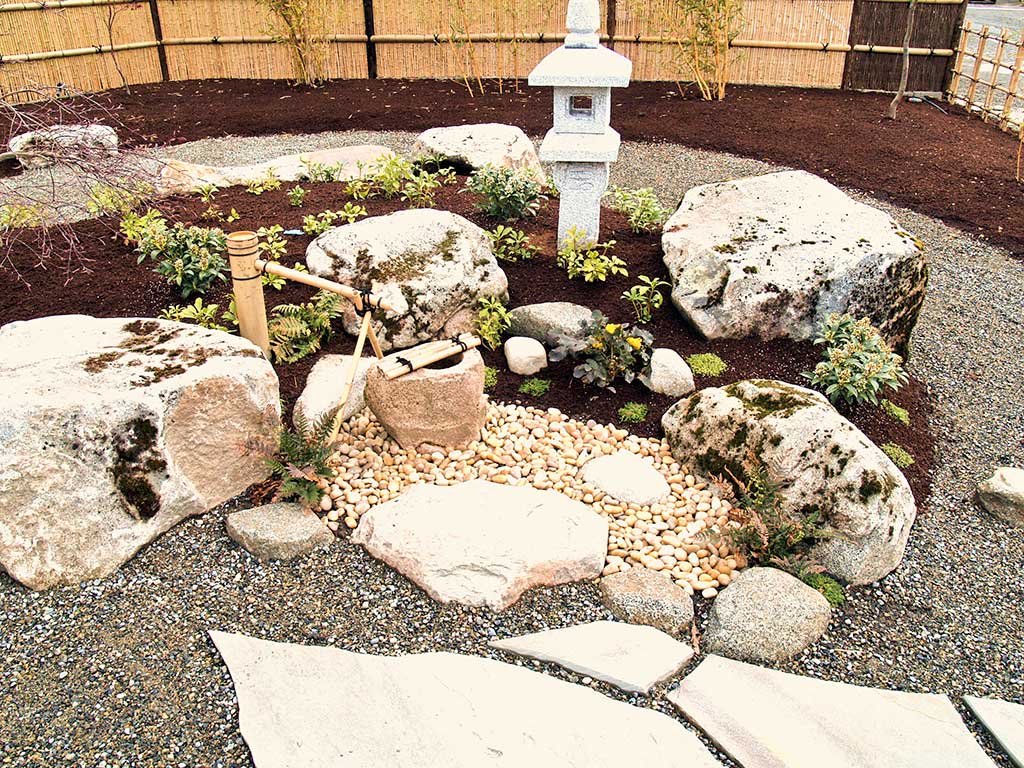 Center of the garden with stone pathway with stone pebbles, stone garden and Japanese stone fountain.